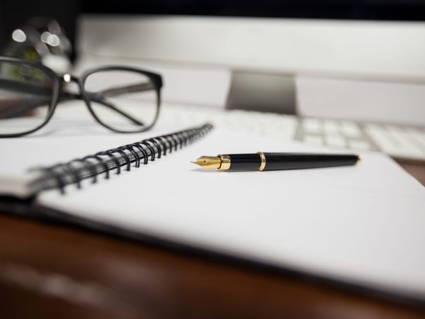 Spiral notepad with pen and reading glasses on a table